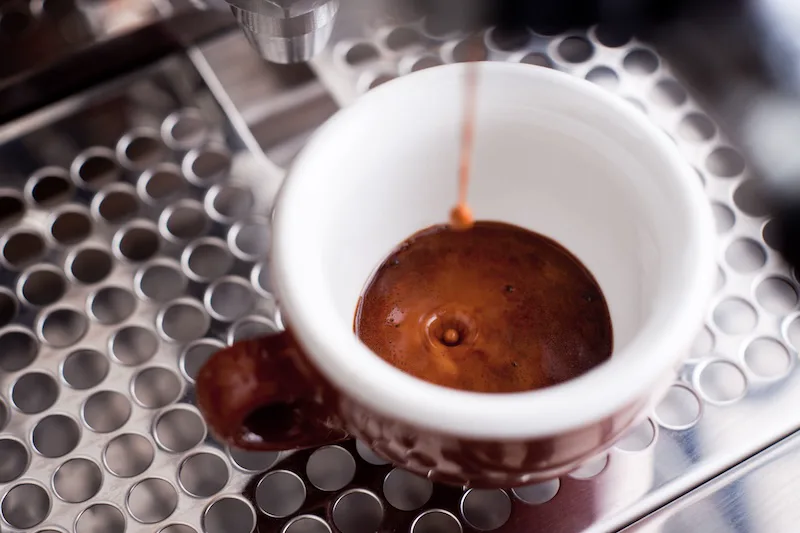 Espresso pouring into a white cup on a machine drip tray